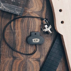 Peut inclure: Gros plan sur une surface en bois avec différents morceaux de bois, dont un manche de guitare, une touche noire et un micro noir avec le texte "T.M.F." dessus.