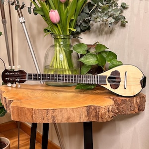 Può includere: Un tavolo in legno con un piano a bordo naturale e gambe in metallo nero. Un mazzo di tulipani rosa e bianchi in un vaso di vetro si trova sul tavolo, insieme a un piccolo strumento musicale a corda in legno.