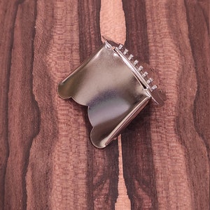 May include: A silver metal cookie cutter shaped like a scalloped edge circle. The cutter has a series of small holes along the top edge.