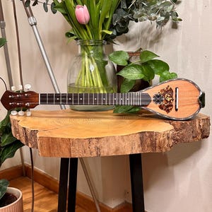Könnte beinhalten: Ein Holztisch mit einem schwarzen Metallgestell, auf dem ein Strauß rosa und weißer Tulpen in einer Glasvase und ein kleines, hölzernes Saiteninstrument stehen.