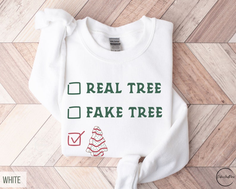 May include: White sweatshirt with the text "REAL TREE" and "FAKE TREE" in green, with a checkmark next to a decorated Christmas tree graphic. The sweatshirt is a Gildan brand.