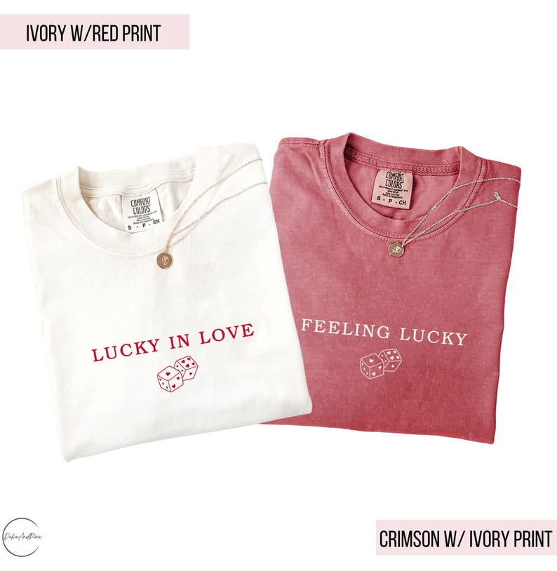 May include: Two t-shirts, one ivory and one crimson, are displayed. The ivory shirt has red text that reads "LUCKY IN LOVE" with dice graphics. The crimson shirt has ivory text that reads "FEELING LUCKY" with dice graphics. Both shirts have a necklace.