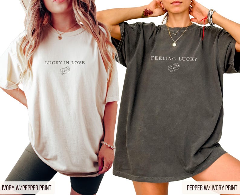 May include: Two t-shirts, one ivory and one pepper, each with a graphic print. The ivory shirt has the text "LUCKY IN LOVE" above a dice graphic. The pepper shirt has the text "FEELING LUCKY" above a dice graphic.