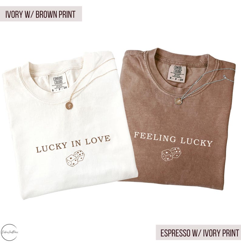 May include: Two t-shirts, one ivory and one espresso, with the text "LUCKY IN LOVE" and "FEELING LUCKY" printed on them. Each shirt has a dice graphic and a gold necklace. The text "IVORY W/ BROWN PRINT" and "ESPRESSO W/ IVORY PRINT" are also visible.