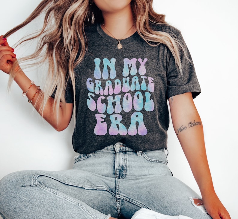May include: A dark grey t-shirt with a tie-dye effect graphic that says "In My Graduate School Era".
