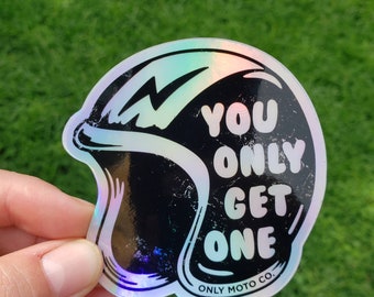 Op de afbeelding: Holografische sticker in de vorm van een motorhelm. De zwarte helm heeft een witte omtrek en een bliksemschicht. De tekst luidt "YOU ONLY GET ONE" en "ONLY MOTO CO."