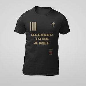 Könnte beinhalten: Schwarzes T-Shirt mit goldenen vertikalen Streifen und einem Kreuz. Der Text "BLESSED TO BE A REF" ist in Gold gedruckt, mit zusätzlichem Text in Rot und Gold darunter. Ein lässiges T-Shirt für Schiedsrichter.