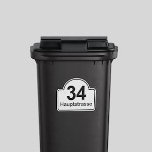 Pode incluir: Lixeira preta com um adesivo branco que diz "34 Hauptstrasse".