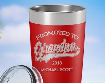 May include: A red stainless steel tumbler with a clear plastic lid. The tumbler features white engraved text that reads PROMOTED TO Grandpa 2018 MICHAEL SCOTT. The base has horizontal ridges and a Polar Camel logo is visible on the lower right.