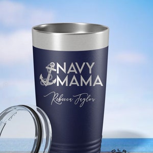 May include: Navy blue stainless steel tumbler with a silver lid and a white anchor and text that reads "Navy Mama" and "Rebecca Taylor".