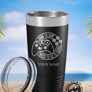 May include: Black and silver stainless steel tumbler with a white design that says "Born to Game Forced to Go to School" with a video game controller graphic. The tumbler has a lid and a personalized name.