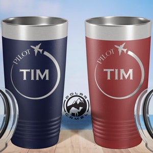 May include: Two stainless steel tumblers with lids. The tumblers are engraved with the words "Pilot Tim" and a small airplane. One tumbler is navy blue and the other is burgundy.
