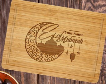 May include: A wooden cutting board with a laser engraved design of a crescent moon, a mosque, and stars. The text "Eid Mubarak" is engraved on the board, along with the words "Your Name".