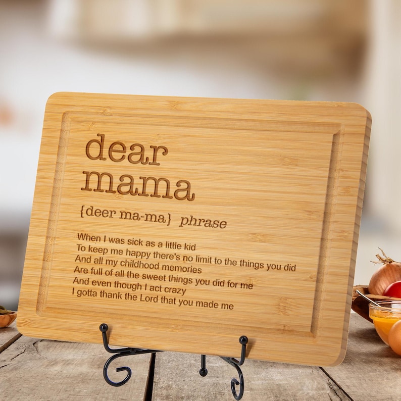 Puede incluir: Tabla de cortar rectangular de bamb&uacute; con las palabras "dear mama" grabadas. Debajo, la frase "{deer ma-ma} phrase" y un poema. La tabla se muestra sobre un soporte de metal negro.