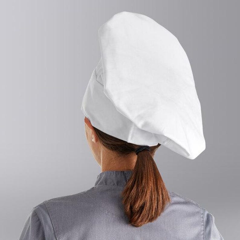 Puede incluir: Un gorro de chef blanco con la parte superior redondeada y un ala ancha. El gorro lo lleva una persona con el pelo largo y casta&ntilde;o recogido en una coleta.