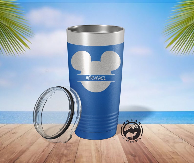 May include: A blue stainless steel tumbler with a Mickey Mouse silhouette and the name "MICHAEL" in a split font. The tumbler has a clear lid and is sitting on a wooden surface.