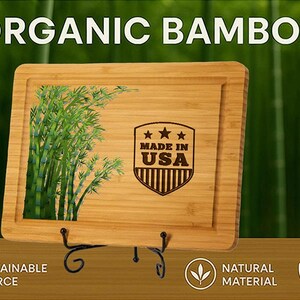 Puede incluir: Tabla de cortar rectangular de bamb&uacute; con borde empotrado, con una ilustraci&oacute;n de planta de bamb&uacute; y un emblema "MADE IN USA". Las palabras "ORGANIC BAMBOO" est&aacute;n en la parte superior. La tabla se muestra sobre un soporte de metal negro.