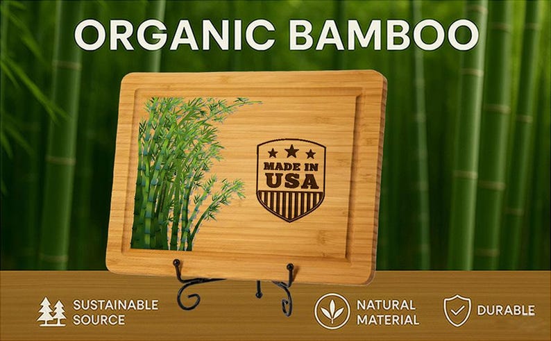 Puede incluir: Tabla de cortar rectangular de bamb&uacute; con borde empotrado, con una ilustraci&oacute;n de planta de bamb&uacute; y un emblema "MADE IN USA". Las palabras "ORGANIC BAMBOO" est&aacute;n en la parte superior. La tabla se muestra sobre un soporte de metal negro.