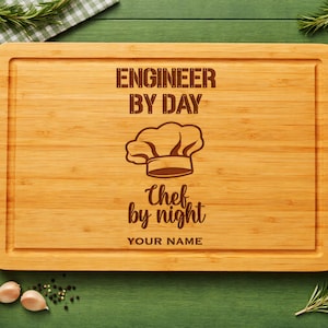 May include: A rectangular bamboo cutting board with a juice groove and laser-engraved text that reads ENGINEER BY DAY, a chef hat icon, the text CHEF by night, and the placeholder text YOUR NAME centered on the wooden surface.