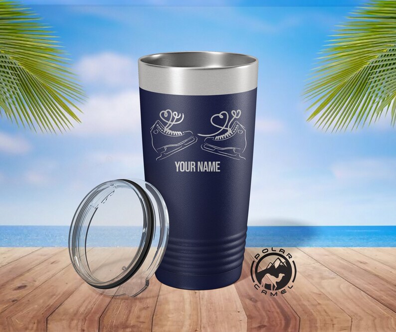 May include: Navy blue insulated tumbler with a silver rim and a clear lid. The tumbler features a white graphic of ice skates with heart-shaped laces and the text "YOUR NAME". The Polar Camel logo is visible.