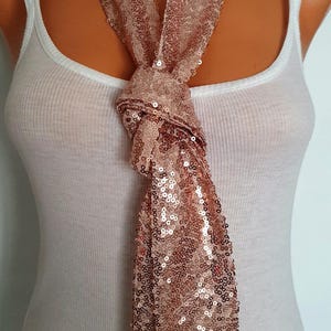May include: A rose gold sequined scarf tied in a bow around a mannequin's neck. The scarf is made of a soft, shimmery fabric and is perfect for adding a touch of glamour to any outfit.
