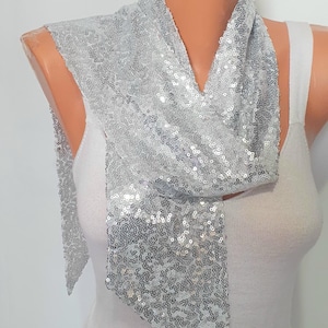 May include: A silver sequin scarf draped over a mannequin. The scarf is made of small, shiny, round sequins and is draped in a scarf style. The background is plain white.