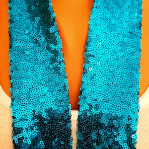 Puede incluir: Una bufanda de lentejuelas turquesa con un degradado de lentejuelas azul oscuro en la parte inferior.