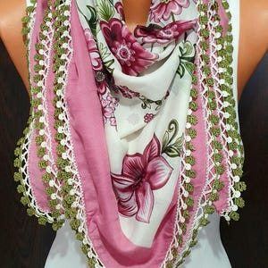 May include: A pink and white floral scarf with green crocheted trim. The scarf is folded and displayed on a white mannequin.