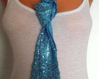 May include: A turquoise sequin scarf is knotted at the chest of a mannequin. The scarf is a vibrant shade of blue and is covered in small, reflective sequins. The mannequin is wearing a white tank top.