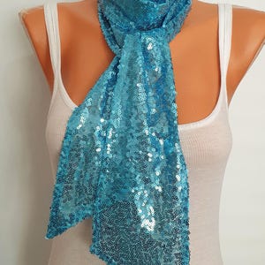 May include: A turquoise blue sequined scarf. The scarf is made of small, shiny sequins and is tied around the neck of a mannequin.
