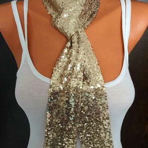 May include: A gold sequined scarf tied in a bow around a white tank top.