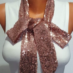 Peut inclure: Un foulard en sequins rose gold noué en nœud papillon autour du cou d'un mannequin. Le foulard est fait de petits sequins brillants.