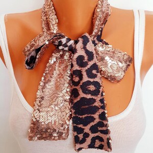 May include: A sequined scarf with a leopard print accent. The scarf is made of bronze-colored sequins and features a leopard print pattern in brown and black. The scarf is tied in a bow.