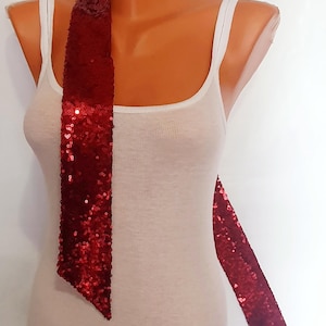 Op de afbeelding: Een rode chokerketting met pailletten en een lange, vloeiende staart. De ketting is om een wit tanktop geknoopt.