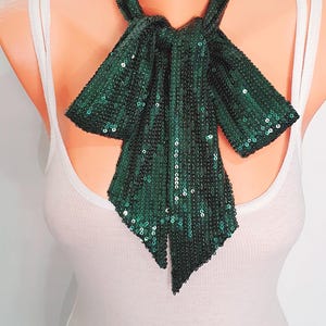 May include: A dark green sequined bow tie, displayed on a mannequin. The bow tie is made of small, shiny sequins and is tied in a classic bow shape. The background is plain white.