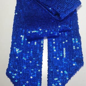 May include: A long, rectangular scarf covered in vibrant royal blue sequins. The fabric is densely embellished with small, reflective circular sequins that create a shimmering texture across the entire surface of the accessory.