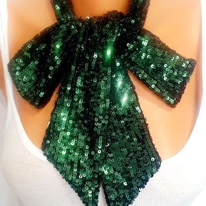 May include: A dark green sequined bow tie. The bow tie is made of small, shiny sequins and is worn around the neck. The bow tie is a formal accessory, often worn with a tuxedo or suit.