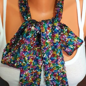 May include: A multi-colored sequin scarf with a bow design. The scarf is made of small, shiny sequins in various colors, including red, blue, green, and yellow. The scarf is worn around the neck and tied in a bow.