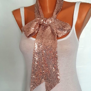 May include: A rose gold sequined scarf tied in a bow. The scarf is made of a soft, shimmery fabric and is perfect for adding a touch of glamour to any outfit.