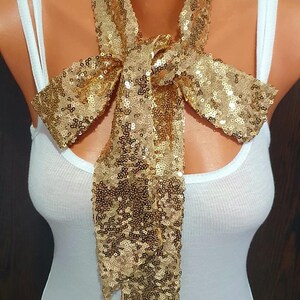 May include: A gold sequined bow tie. The bow tie is tied in a knot and is hanging from a white tank top.