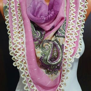 May include: A pink scarf with a paisley print and white crocheted trim. The scarf is folded and draped over a mannequin.