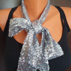 May include: A silver sequined scarf tied in a bow around the neck. The scarf is made of a soft, shimmery fabric and is perfect for adding a touch of sparkle to any outfit.