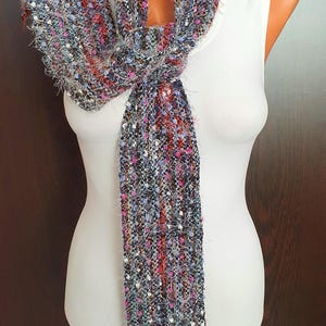 Puede incluir: Una bufanda larga y colorida con una textura peluda. La bufanda está hecha de una mezcla de colores, incluyendo azul, rosa, rojo y blanco. Está atada alrededor del cuello de un maniquí blanco.
