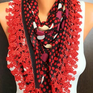 May include: A black scarf with red polka dots and a red lace trim. The scarf is draped around a mannequin. The scarf's pattern includes red, white, and maroon dots.