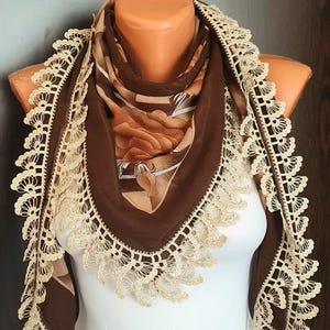 May include: A brown and beige patterned scarf with a crocheted lace trim. The scarf is displayed on a white mannequin.