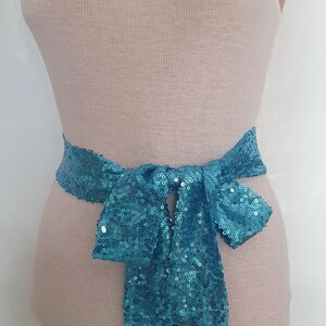 May include: A white tank top with a turquoise sequined belt tied in a bow.