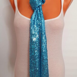 May include: A turquoise blue sequined scarf tied around a mannequin's neck. The scarf is long and flowing, with a slight sheen.