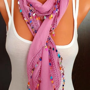 May include: A pink scarf with a crocheted border and colorful sequins. The scarf is draped around a mannequin's neck.