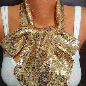 May include: A gold sequined bow tie. The bow tie is made of small, shiny sequins and is tied in a classic bow shape.