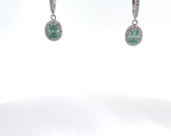 Peut inclure: Une paire de boucles d'oreilles pendantes en argent avec une pierre ovale verte entourée d'un halo de petites pierres blanches.